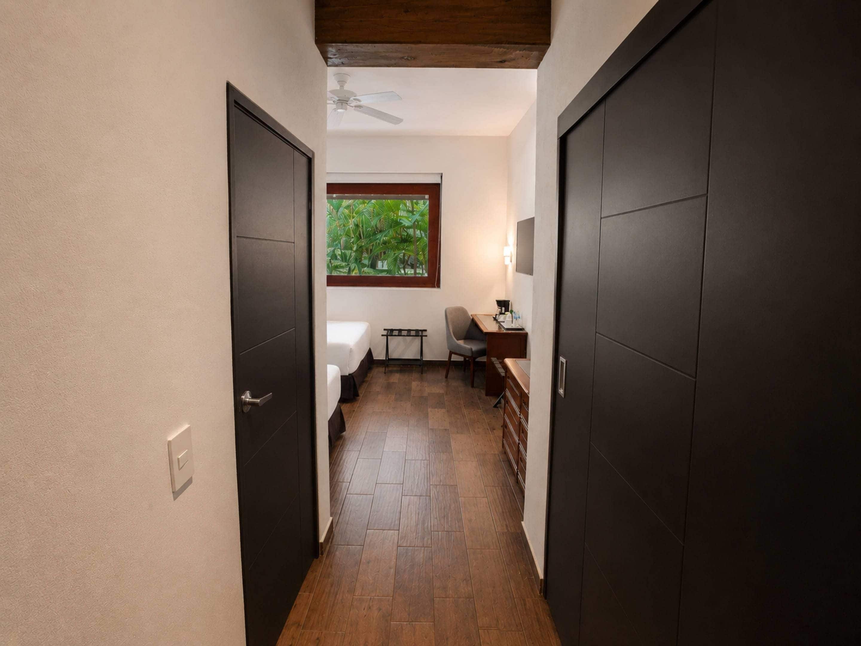Un pasillo estrecho con suelo de madera, un ventilador de techo y una ventana con vistas al verdor.