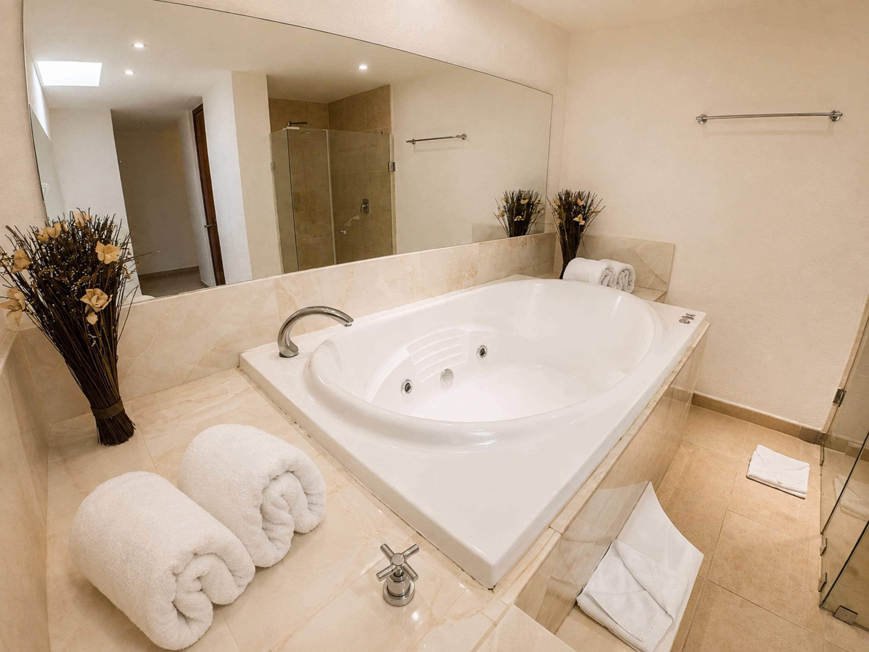A modern bathroom with a large bathtub, a mirror, and two towels.