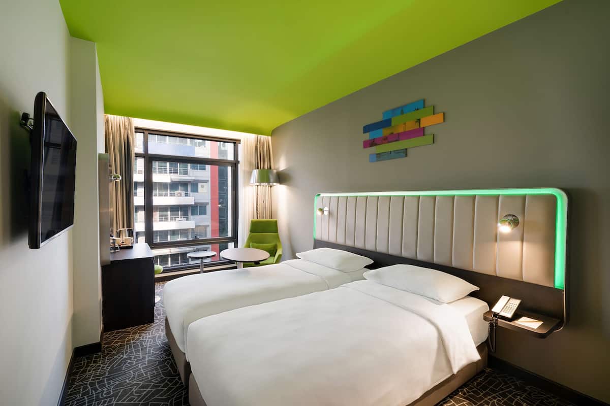 A hotel room with a large bed, a desk with a chair, a TV, and a window with curtains.