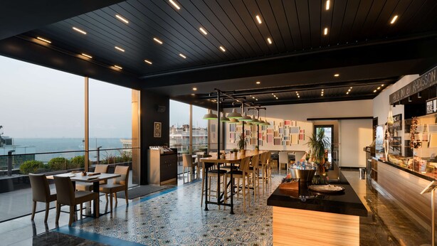 Un espace bar moderne offrant une vue sur la ville, avec un sol à motifs et différents types d’aménagements pour s’asseoir.