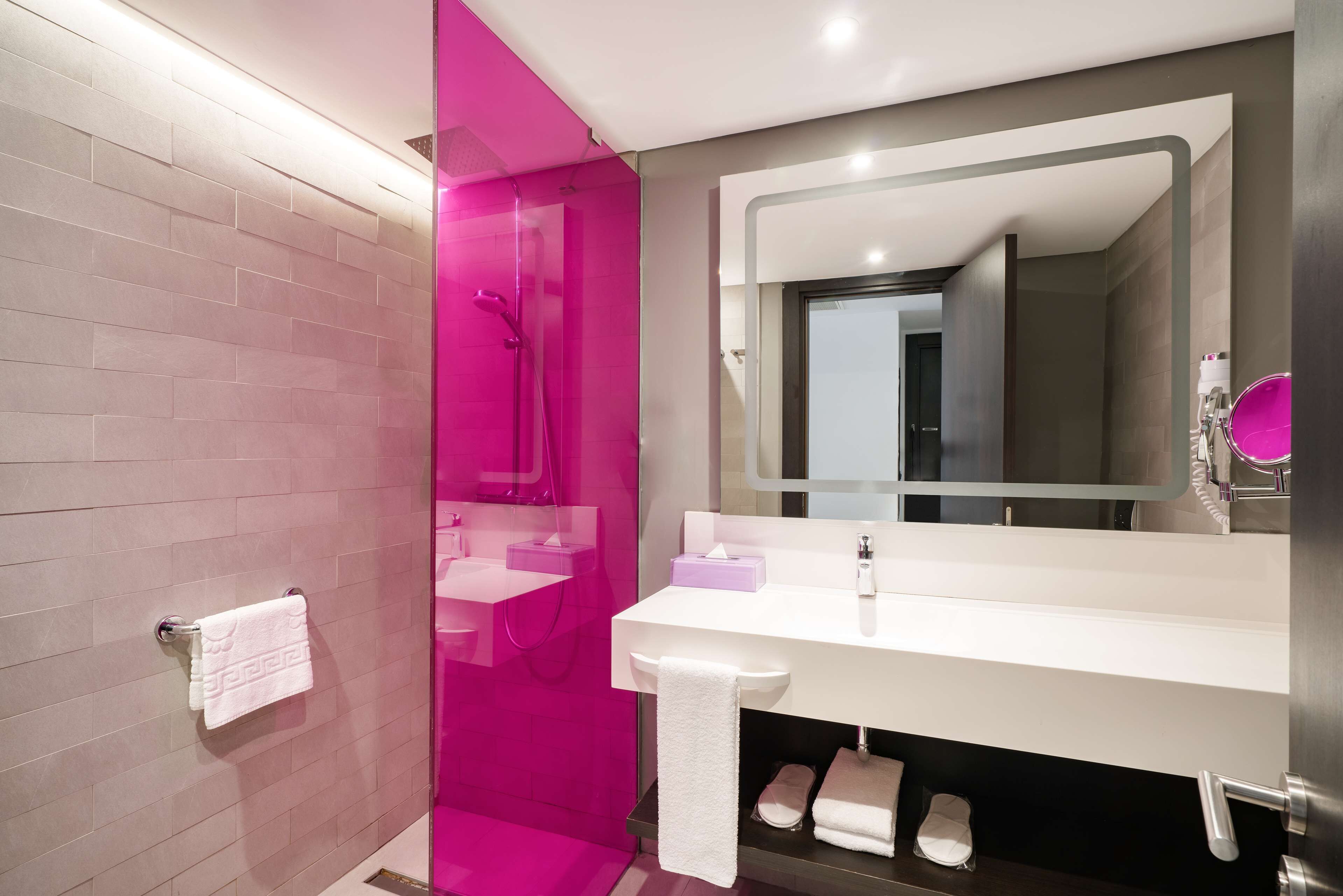 A modern bathroom with a pink shower area, a white sink with a mirror, and a towel rack.