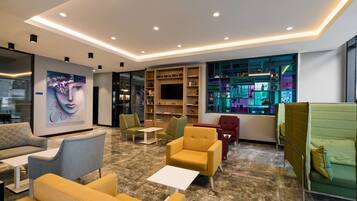 A modern lounge area with seating, a large artwork, a bookshelf, and a television.