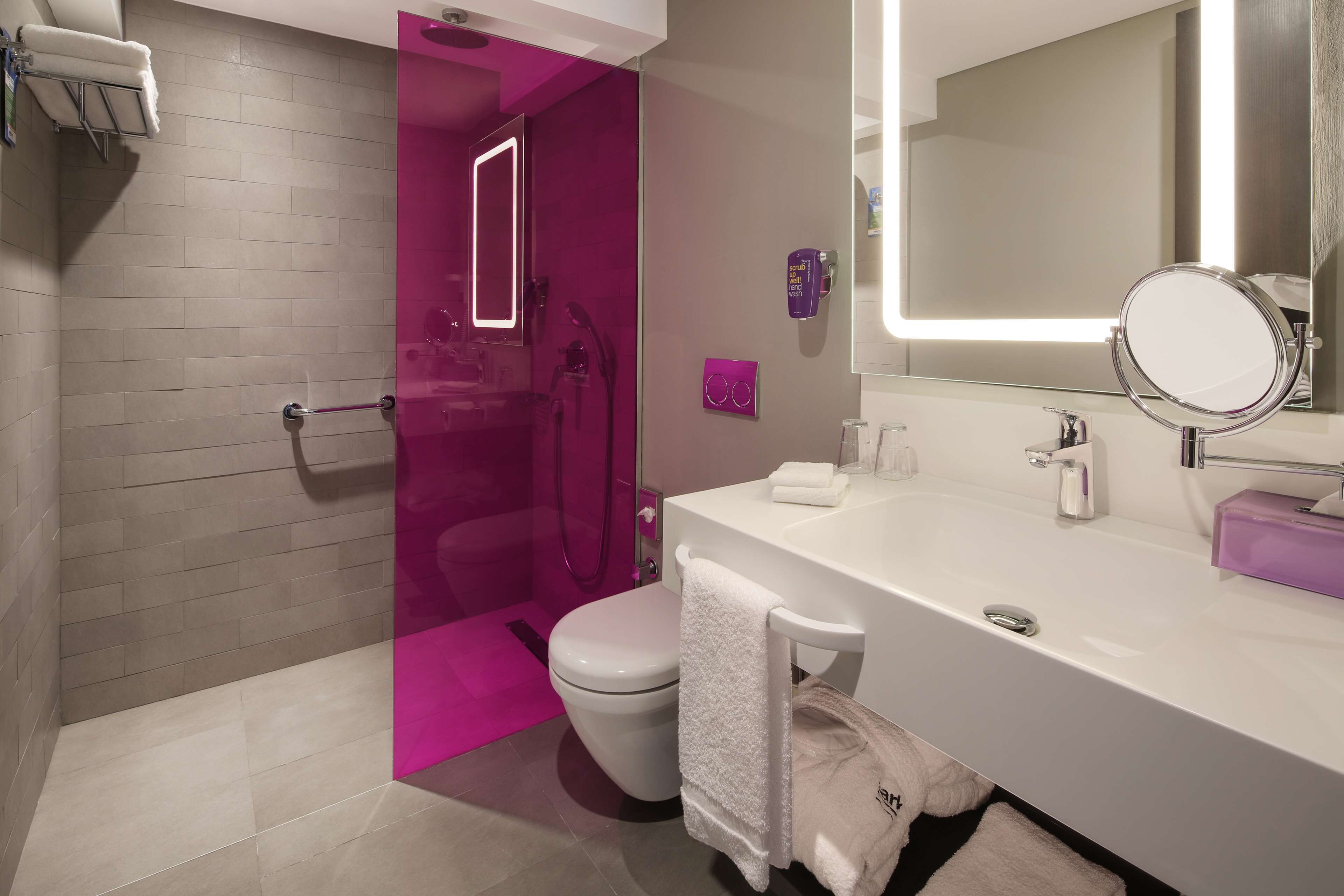 A modern bathroom with a white sink, a large mirror, and a shower area with a pink accent wall.