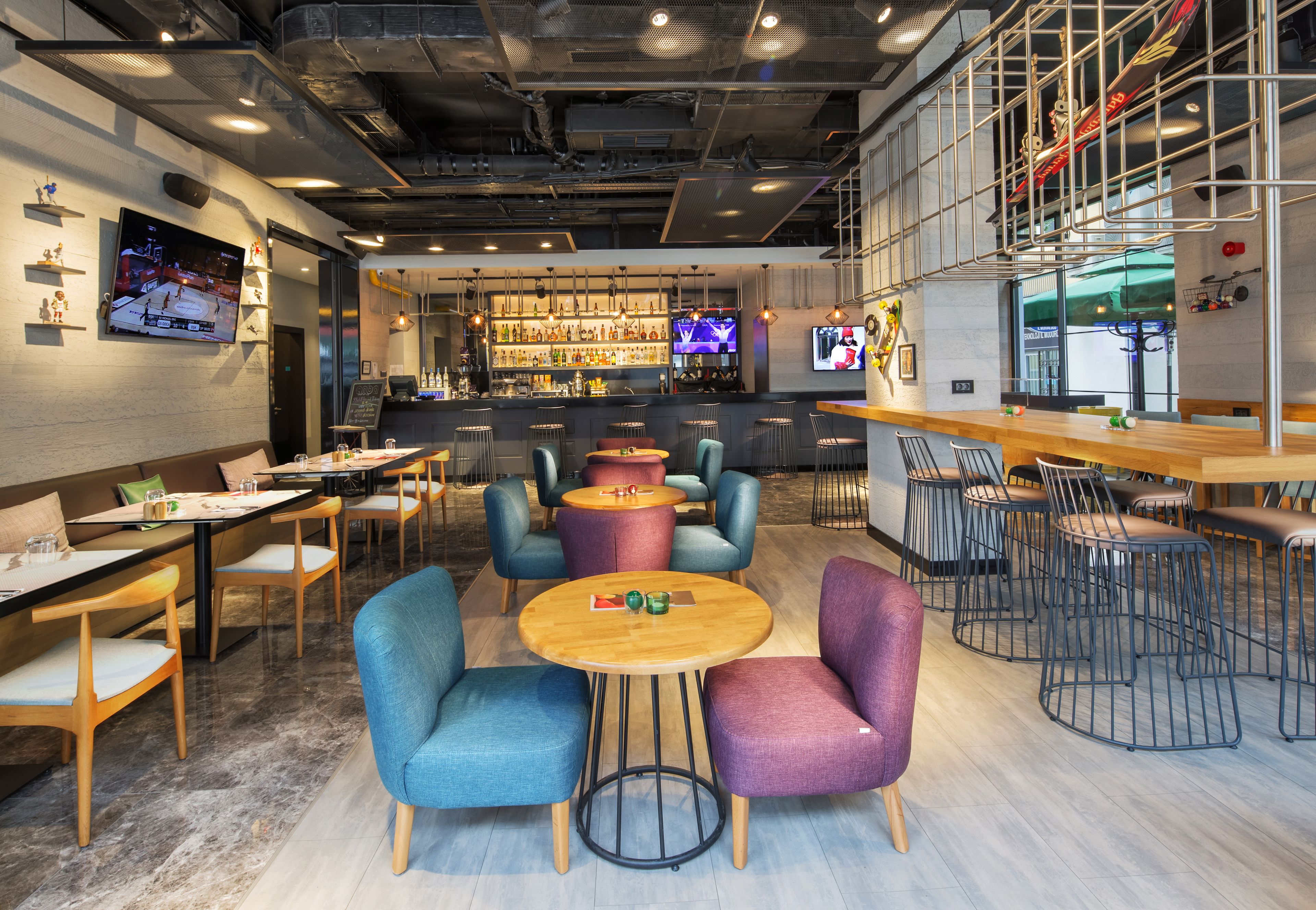 Un espace bar moderne, doté de différents types de sièges, notamment des tables et des chaises rondes, ainsi qu’un écran de télévision diffusant un événement sportif.
