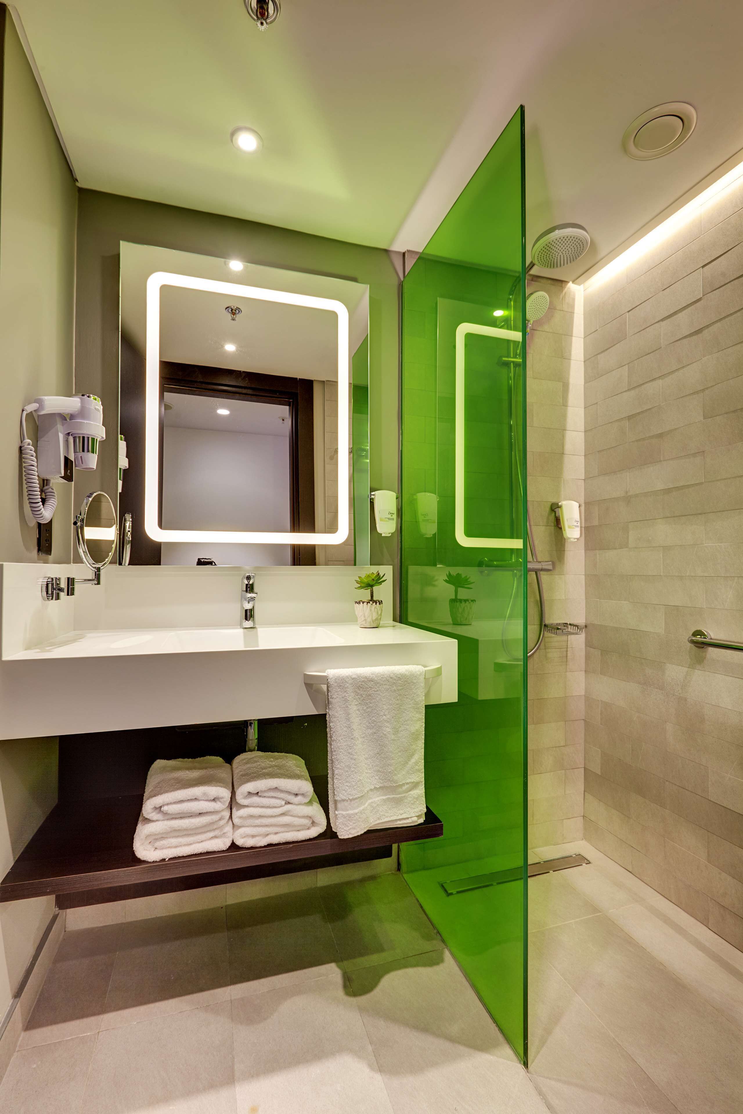 A modern bathroom with a glass shower enclosure, a large mirror with integrated lighting, a white sink, and neatly folded towels.
