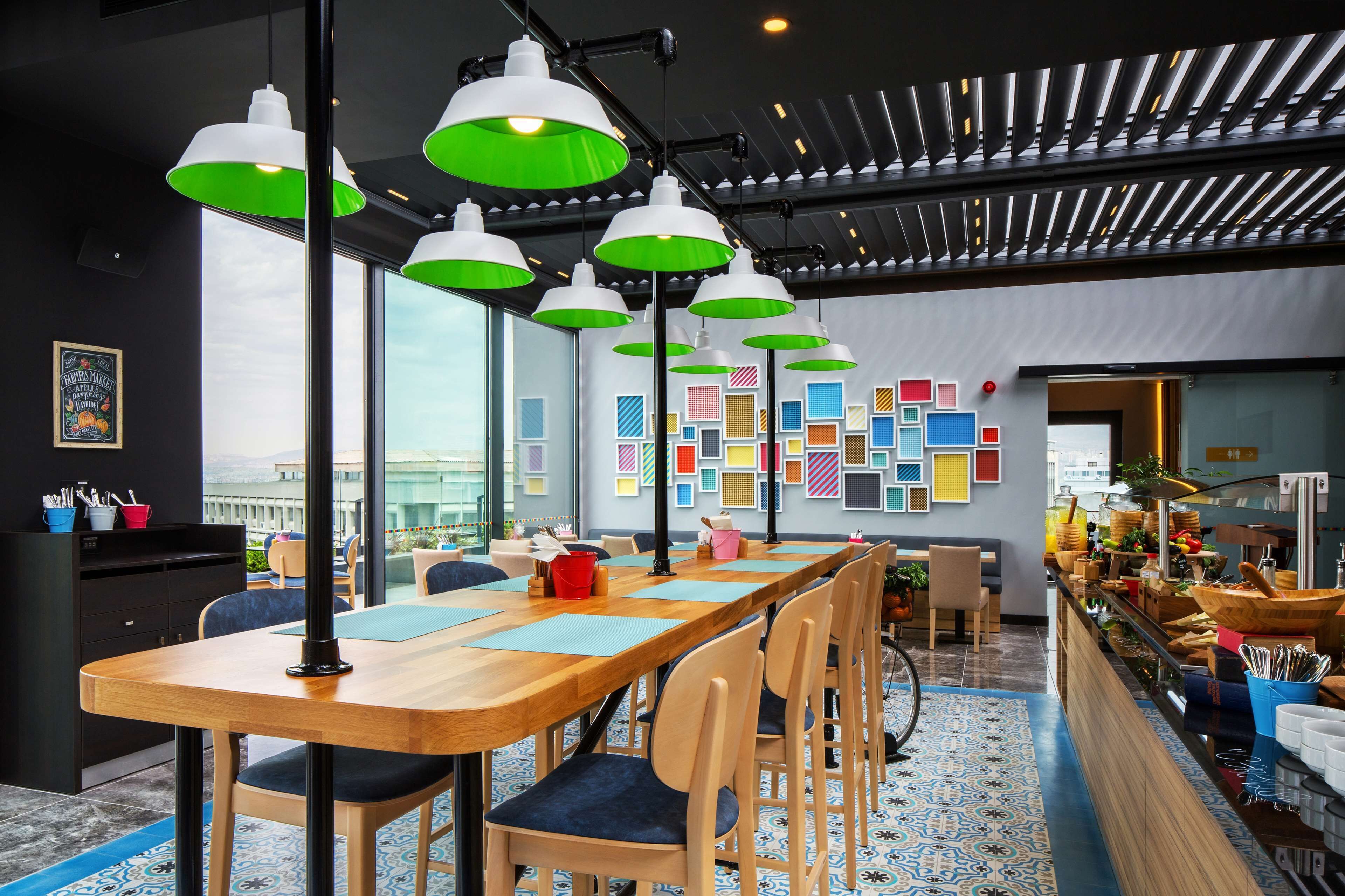 A modern dining area with a long wooden table, multiple chairs, and green pendant lights.