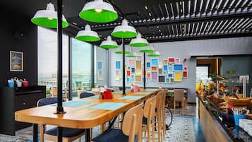 A modern dining area with a long wooden table, multiple chairs, and green pendant lights.