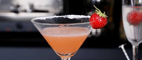 A cocktail in a martini glass with a strawberry garnish, placed on a reflective surface.