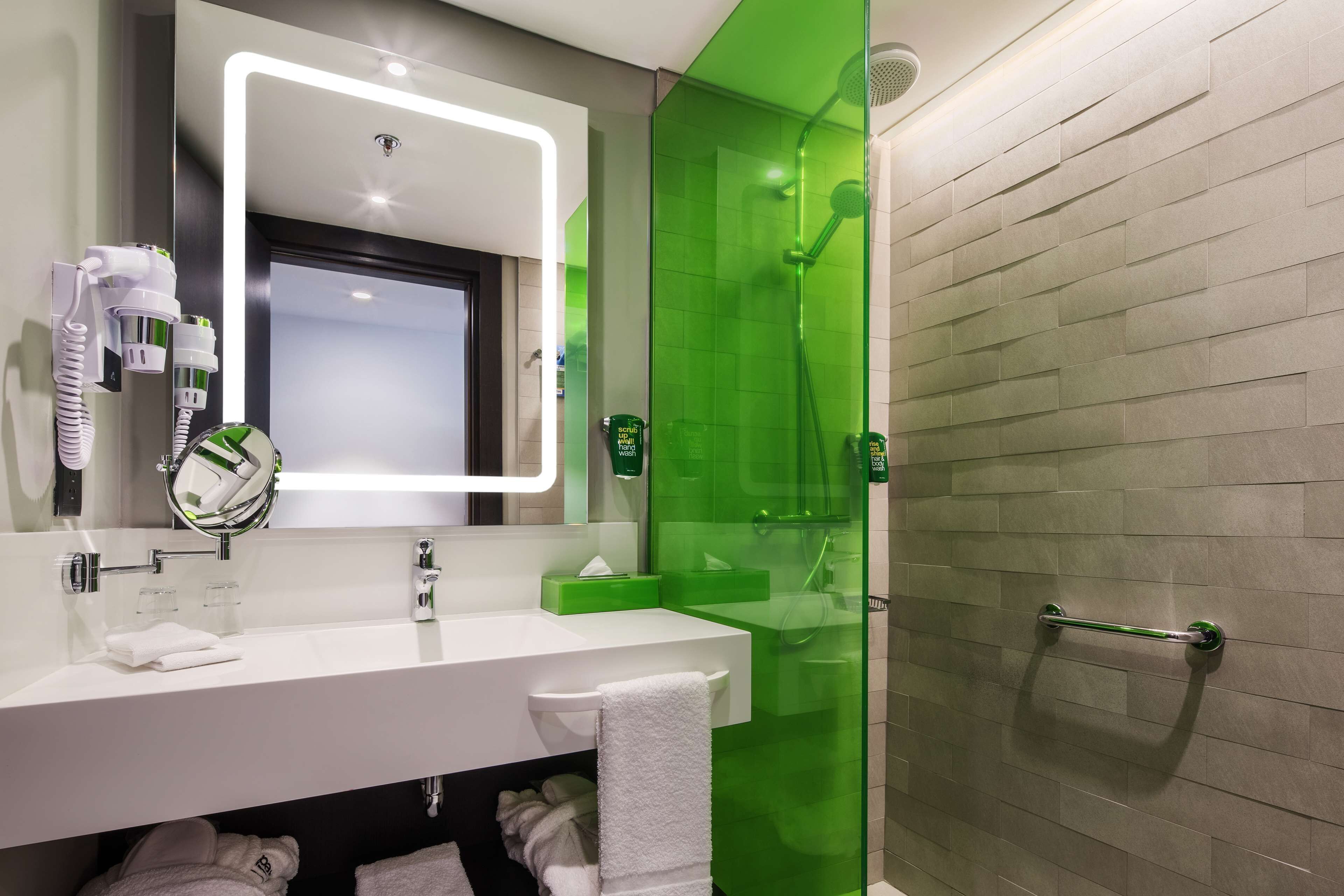 A modern bathroom with a white sink, mirror, and green shower enclosure.