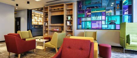 A modern lounge area with comfortable seating, a large bookshelf, and a television.
