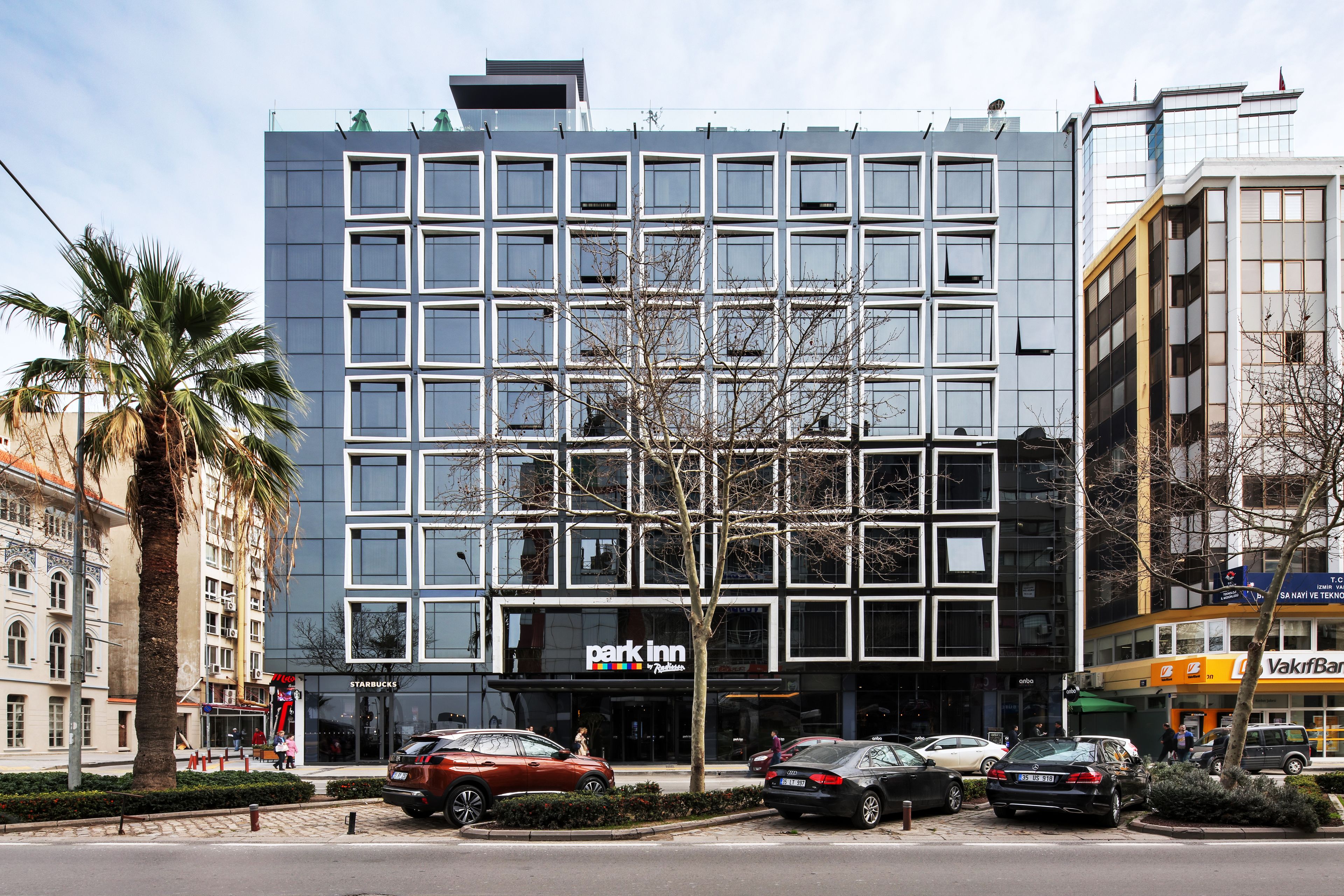 A modern building with a 'Park Inn' sign, multiple parking spaces, and a 'Starbucks' across the street.