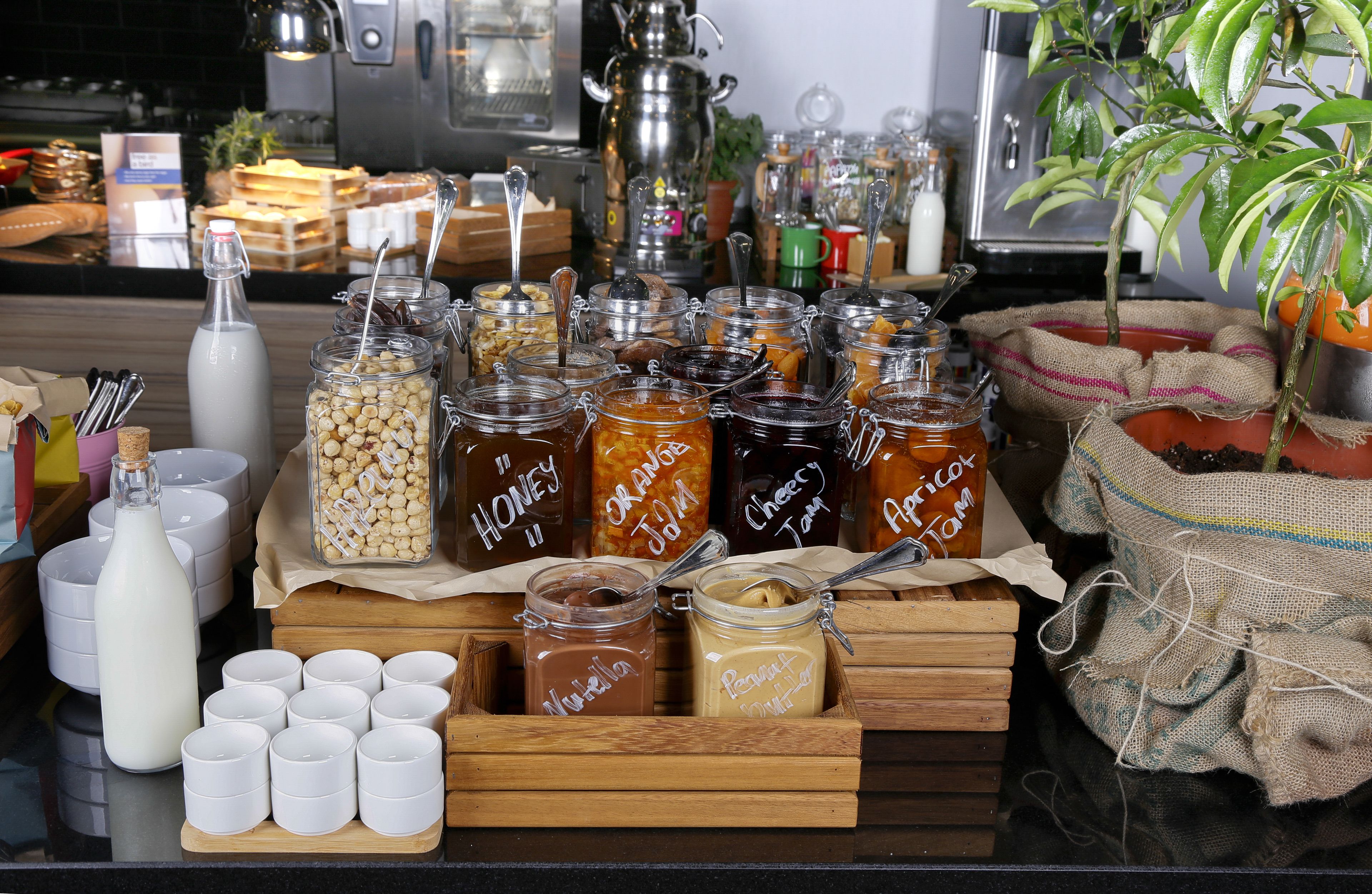 A variety of food items and condiments displayed on a wooden table, including jars of honey, jam, and peanut butter.