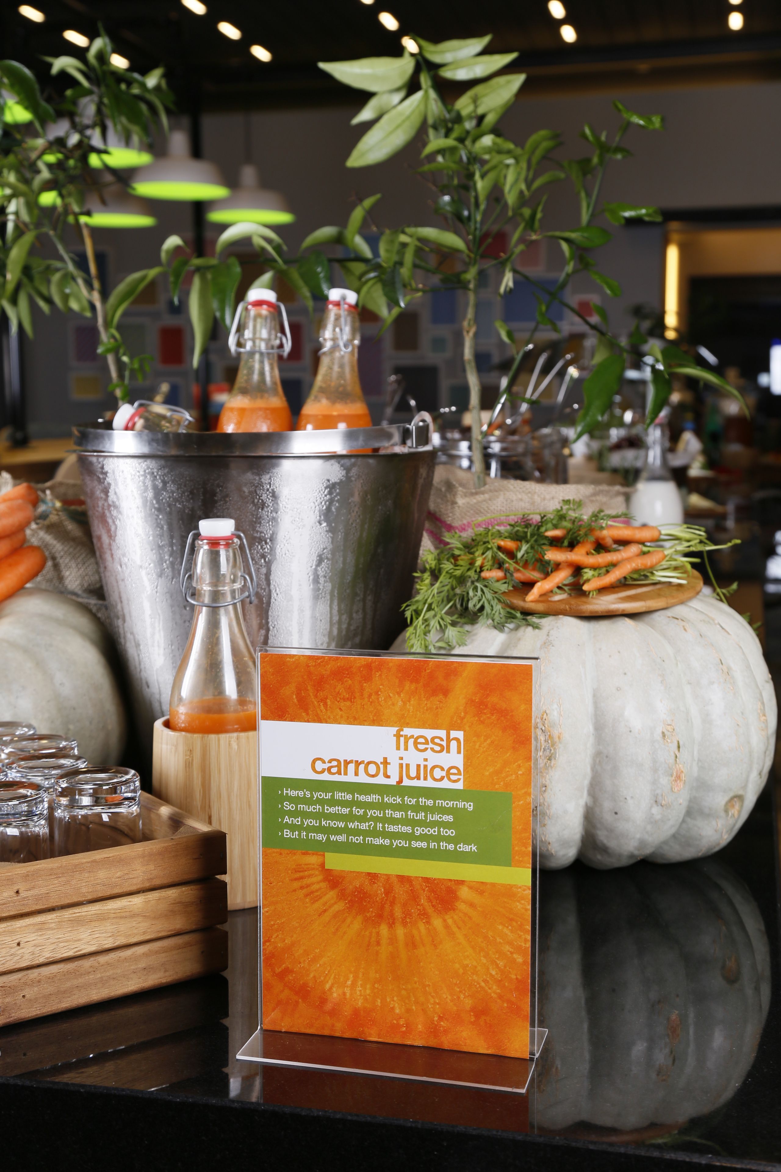 A buffet table with a sign for fresh carrot juice, a metal bucket, and a white pumpkin.