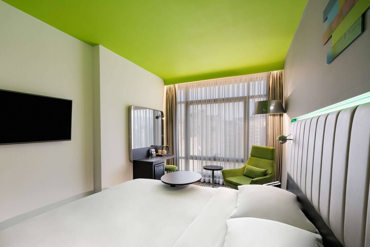 A hotel room with a bed, a desk, a chair, and a window with curtains.