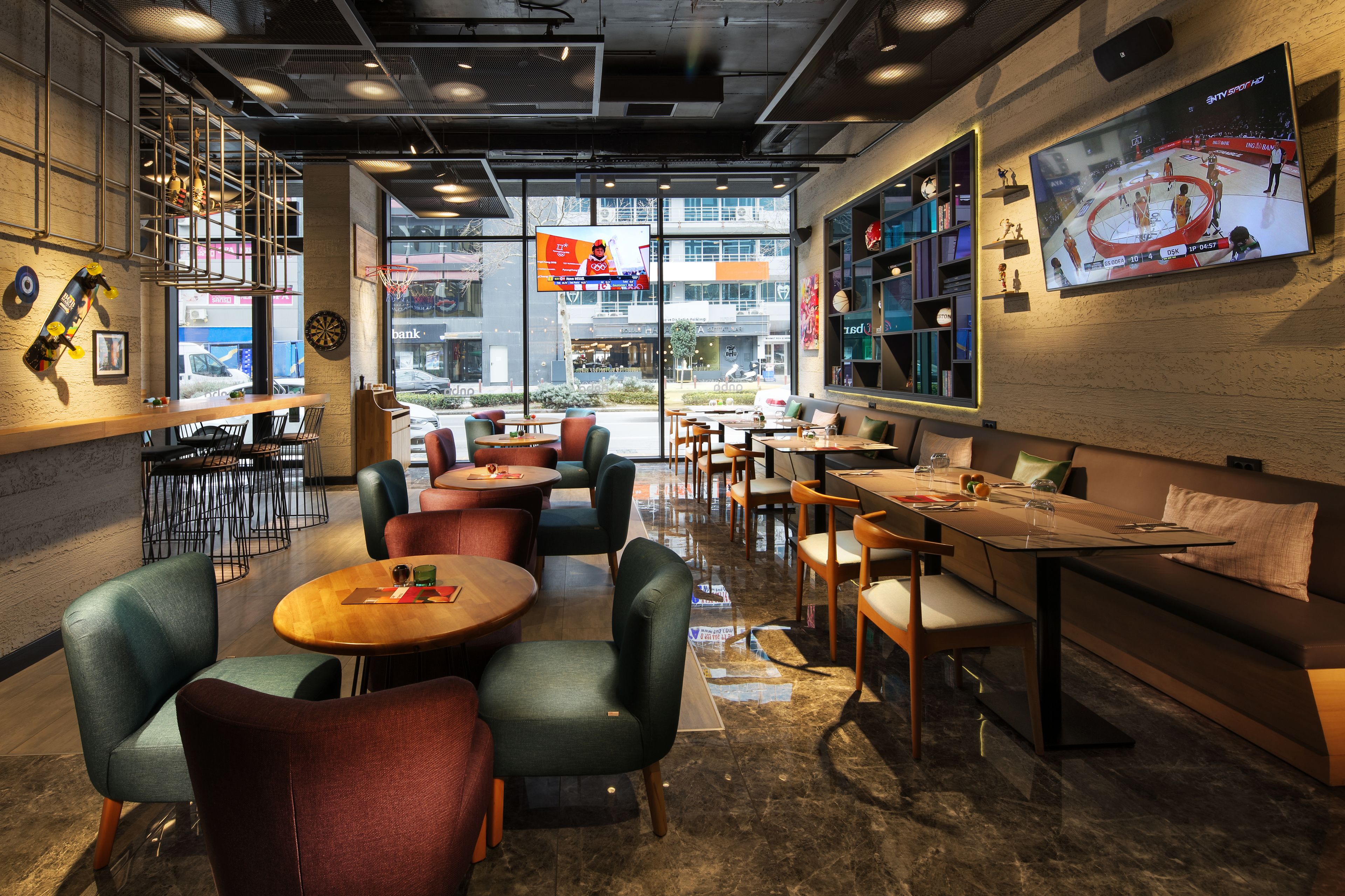 A modern cafe with round tables and chairs, a large TV screen, and a view of the street outside.