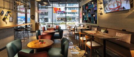 A modern cafe with round tables and chairs, a large TV screen, and a view of the street outside.