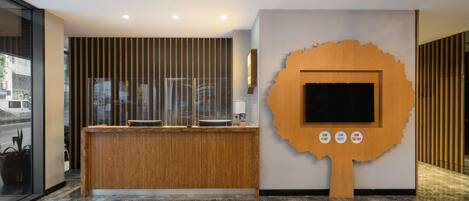 Una zona de recepción con un mostrador de madera, una gran pantalla con forma de árbol y un panel de vidrio.
