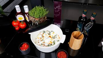 Una encimera de cocina con un tazón de comida decorado con hierbas, tomates y chiles. Hay botellas de salsa y un portalápices de madera.