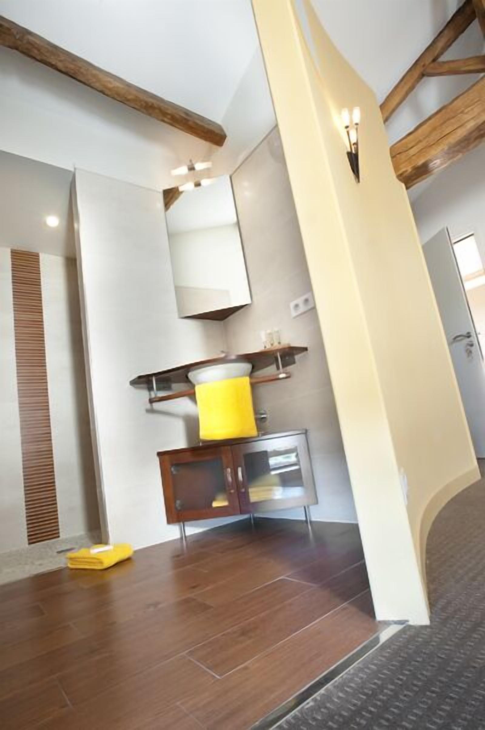 Un baño moderno con vigas de madera, una toalla amarilla y un espejo.
