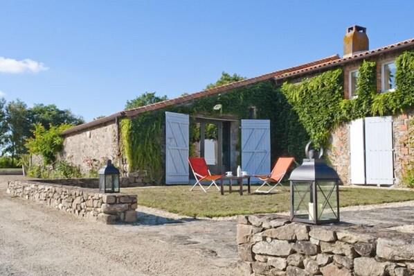 A stone building with a tiled roof, ivy-covered walls, and a small patio area with two chairs and a table. - La Villa des Forges (Lege)