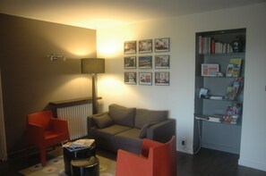 A living room with a sofa, two red chairs, a lamp, a radiator, and a bookshelf with books and framed pictures. - La Villa des Forges (Lege)