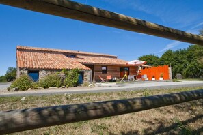 A two-story building with a tiled roof, a stone facade, and a small attached structure with a blue door. - La Villa des Forges (Lege)