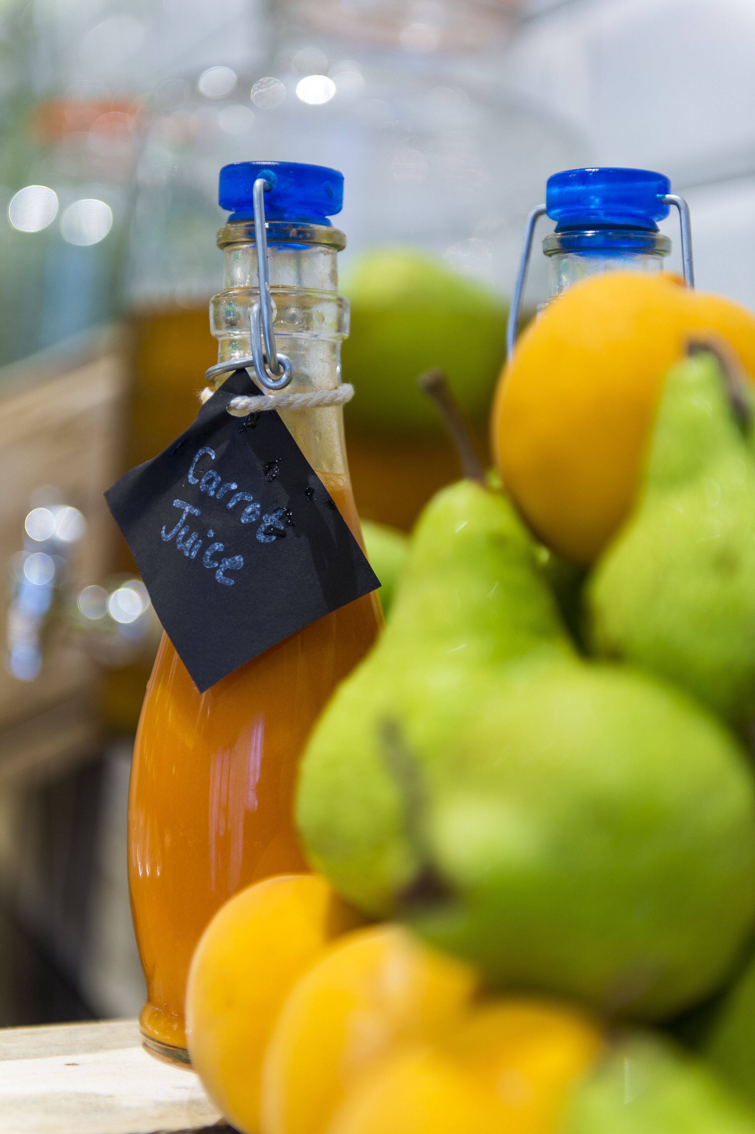 Un vaso de jugo de zanahoria con una etiqueta, rodeado de peras y naranjas.