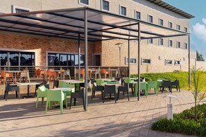 An outdoor patio with tables and chairs, a covered seating area, and a building with large windows and a brick facade. - Park Inn by Radisson Polokwane (Polokwane)