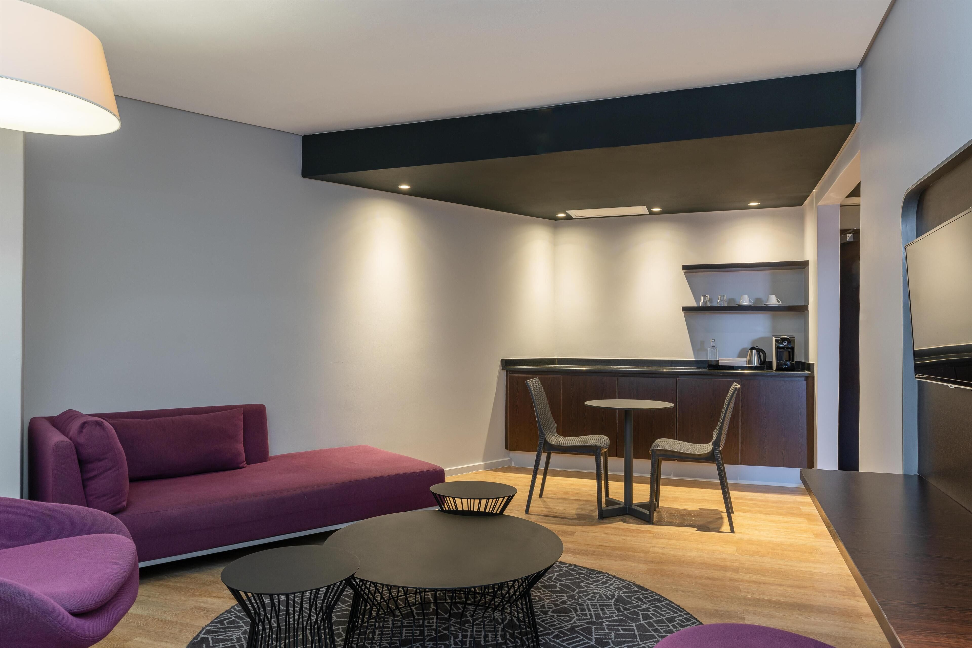 A modern living room with a sofa, two chairs, a coffee table, and a kitchen area with a counter and chairs.
