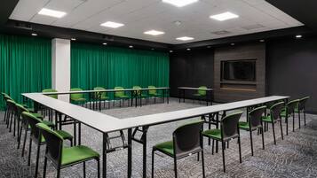 Un salón de conferencias con una larga mesa y sillas, cortinas verdes y una pantalla para proyector.