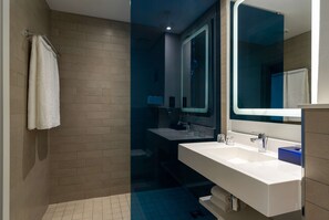A modern bathroom with a large mirror, a white sink, and a shower area. - Park Inn by Radisson Polokwane (Polokwane)