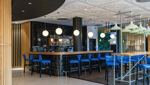 A modern bar area with a wooden counter, blue bar stools, and a patterned ceiling.