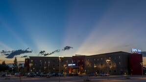 A multi-story hotel with a prominent 'Park Inn' sign, a parking lot with several cars, and a clear sky.