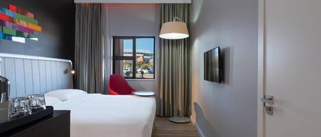 A hotel room with a bed, a red chair, a TV, and a window with a view of a bridge.