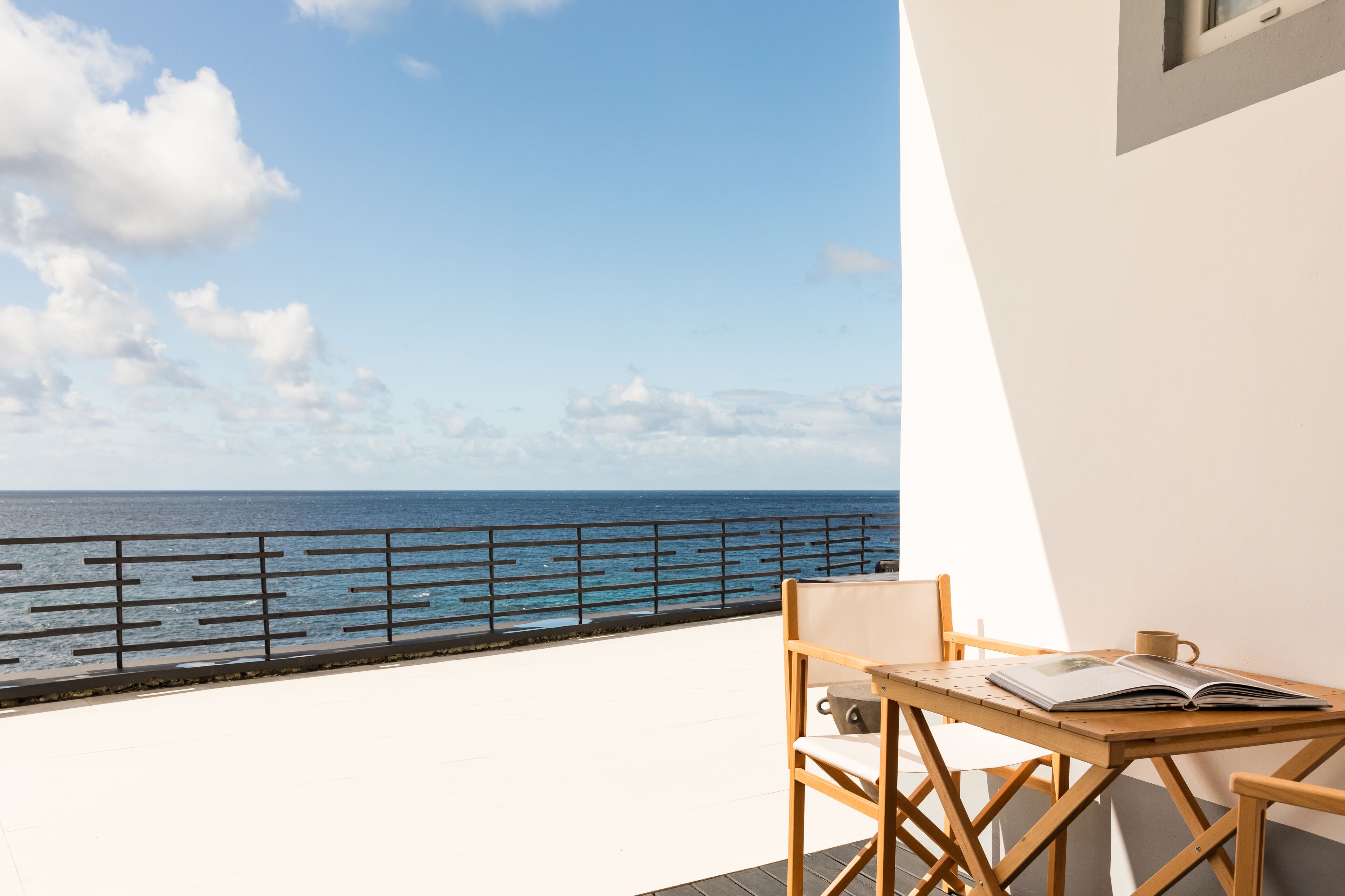 Un balcón con vistas al océano, una mesa con una silla y un libro abierto.