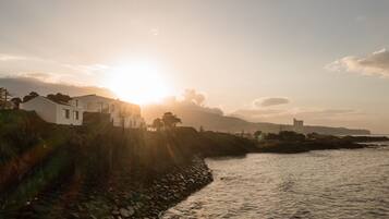 A coastal scene with a stone wall and a white building by the water during sunset.