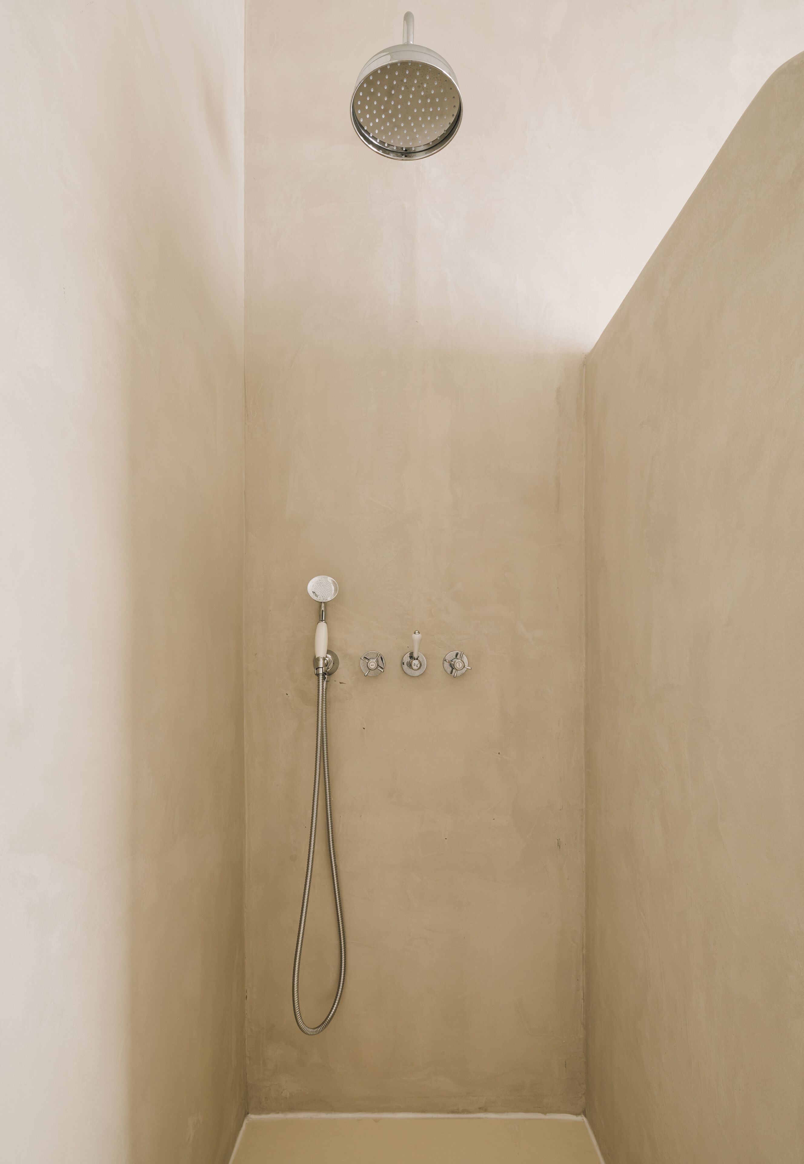 Un pequeño baño con azulejos color beige, ducha de mano y grifo en la pared.