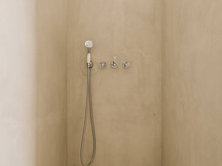 Un pequeño baño con azulejos color beige, ducha de mano y grifo en la pared.