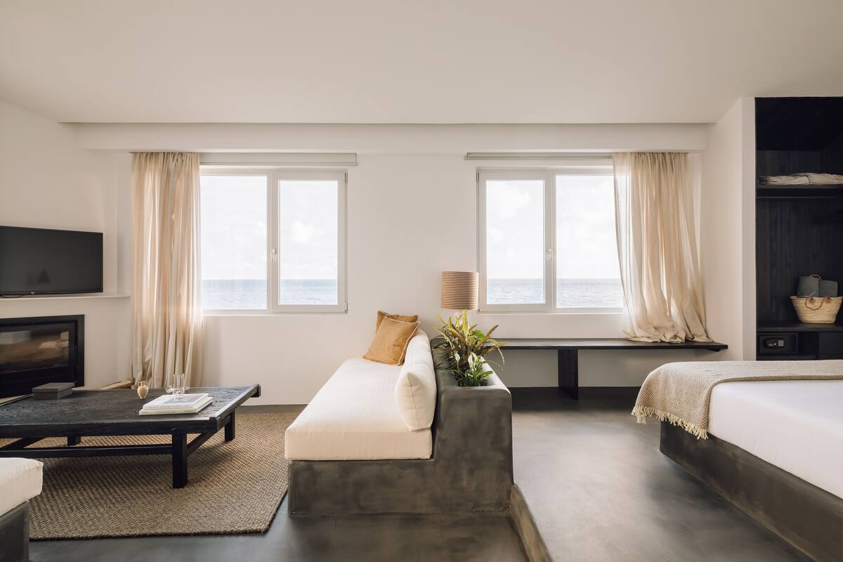 A modern hotel room with a sofa, a bed, a TV, and a large window with curtains.
