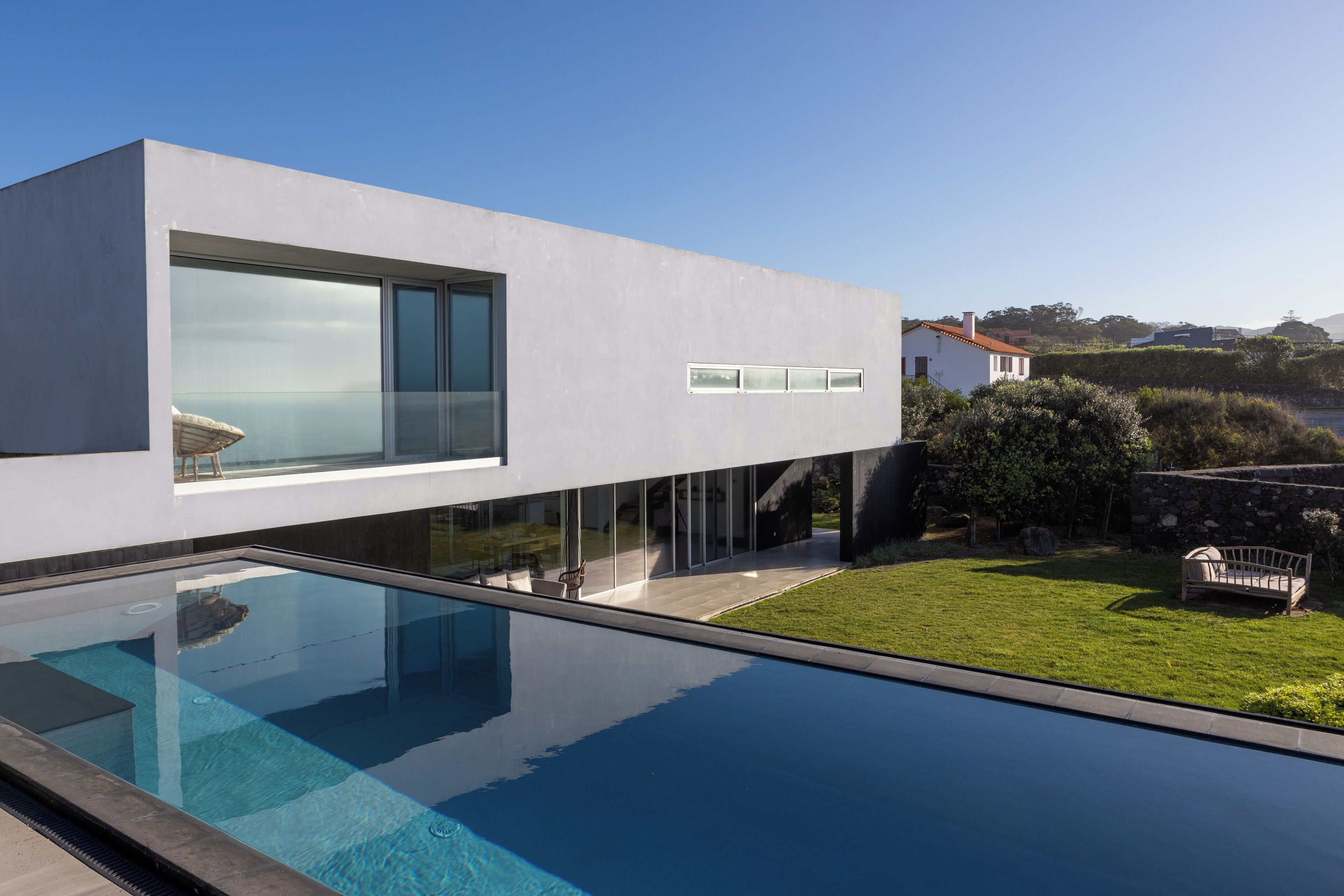 Una casa moderna amb una piscina coberta de vidre, un jardí ben cuidat i vista al mar.