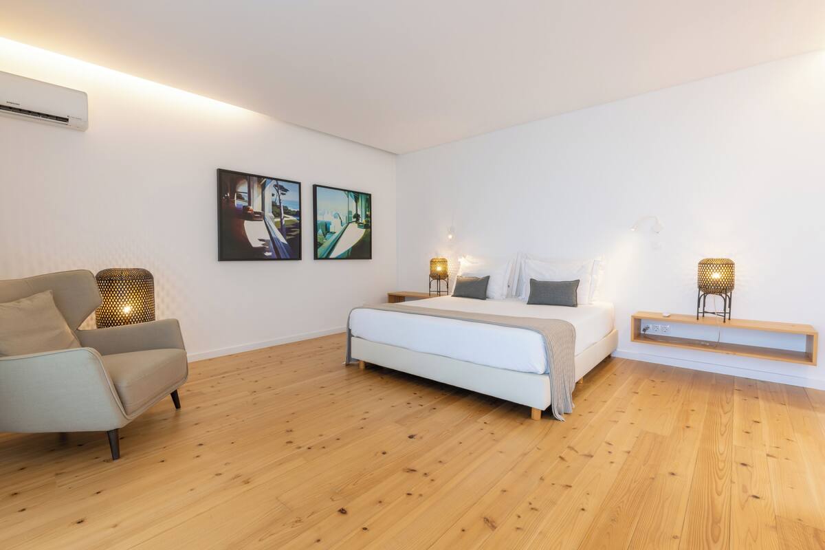 A bedroom with a bed, a chair, two wall-mounted lamps, and two framed pictures.