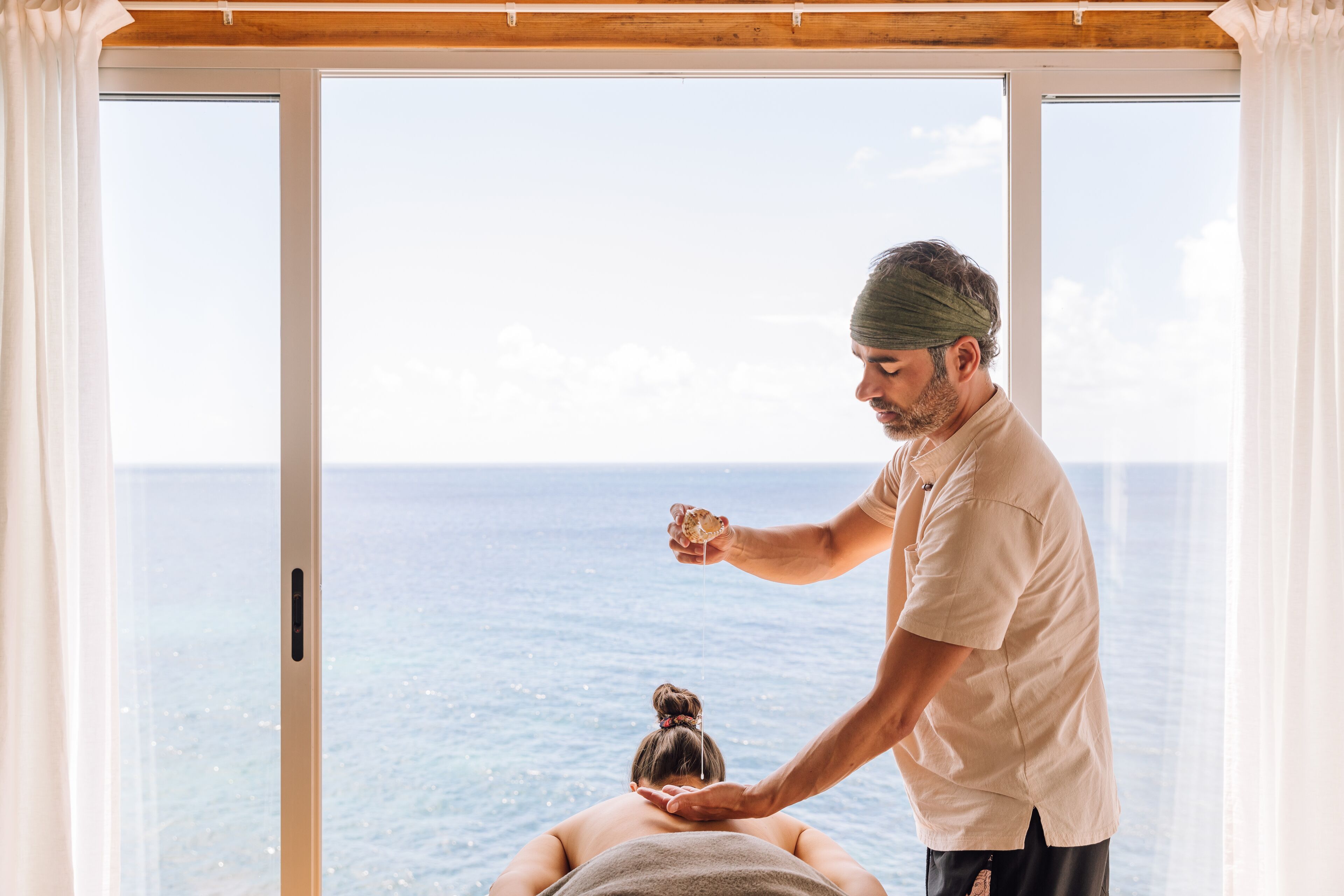 Uma pessoa recebendo massagem com vista para o oceano através de um grande painel de vidro.