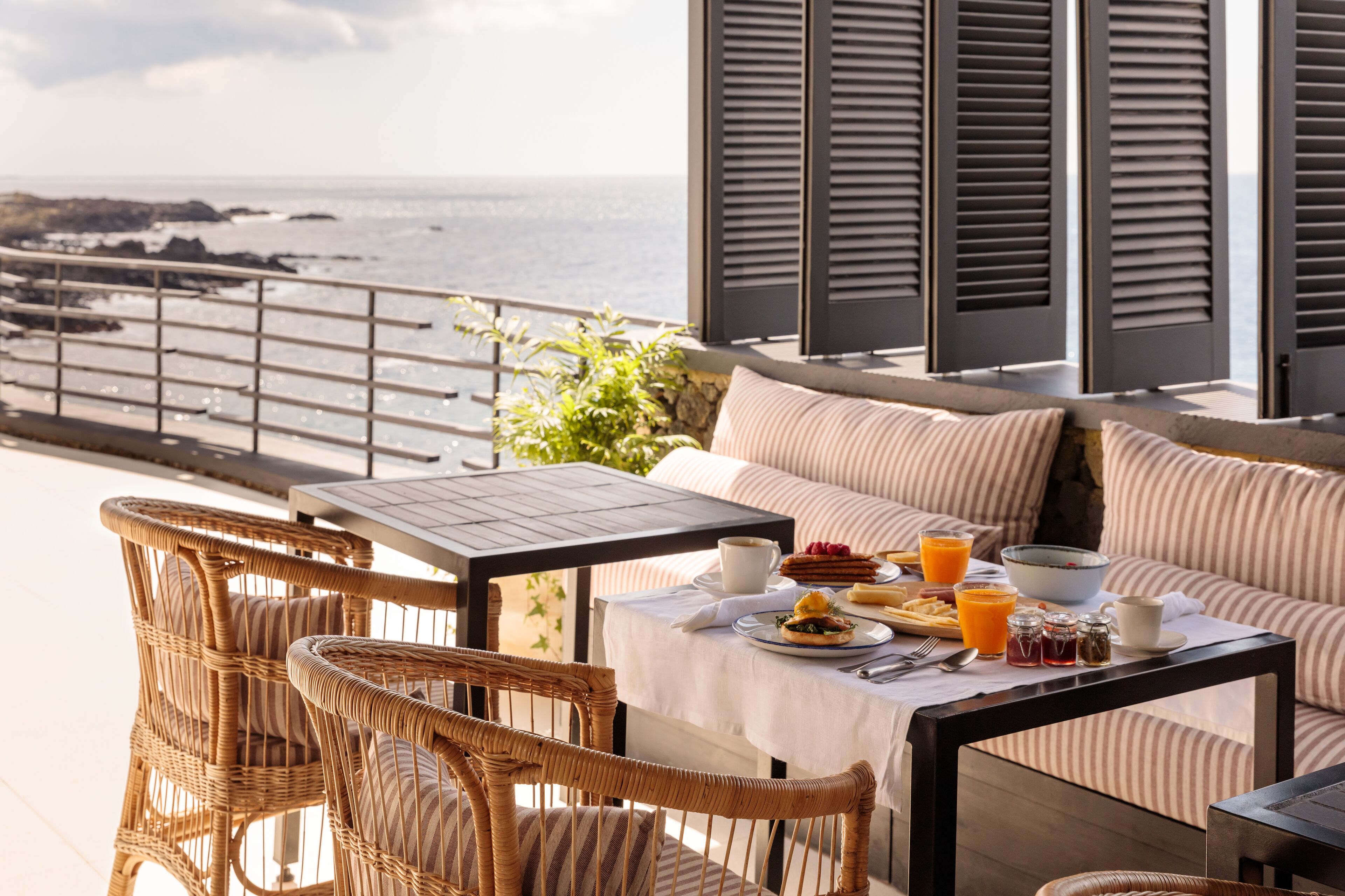 Un balcón con sillas de mimbre y una mesa preparada para el desayuno, con vista al mar.