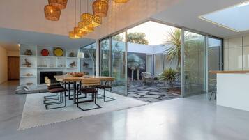 A modern interior with a dining area, white shelves with decorative items, and a glass door leading to a garden.