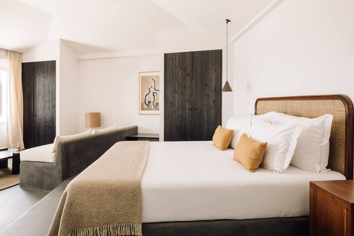 A modern hotel room with a large bed, a sofa, a wooden wardrobe, and a painting on the wall.