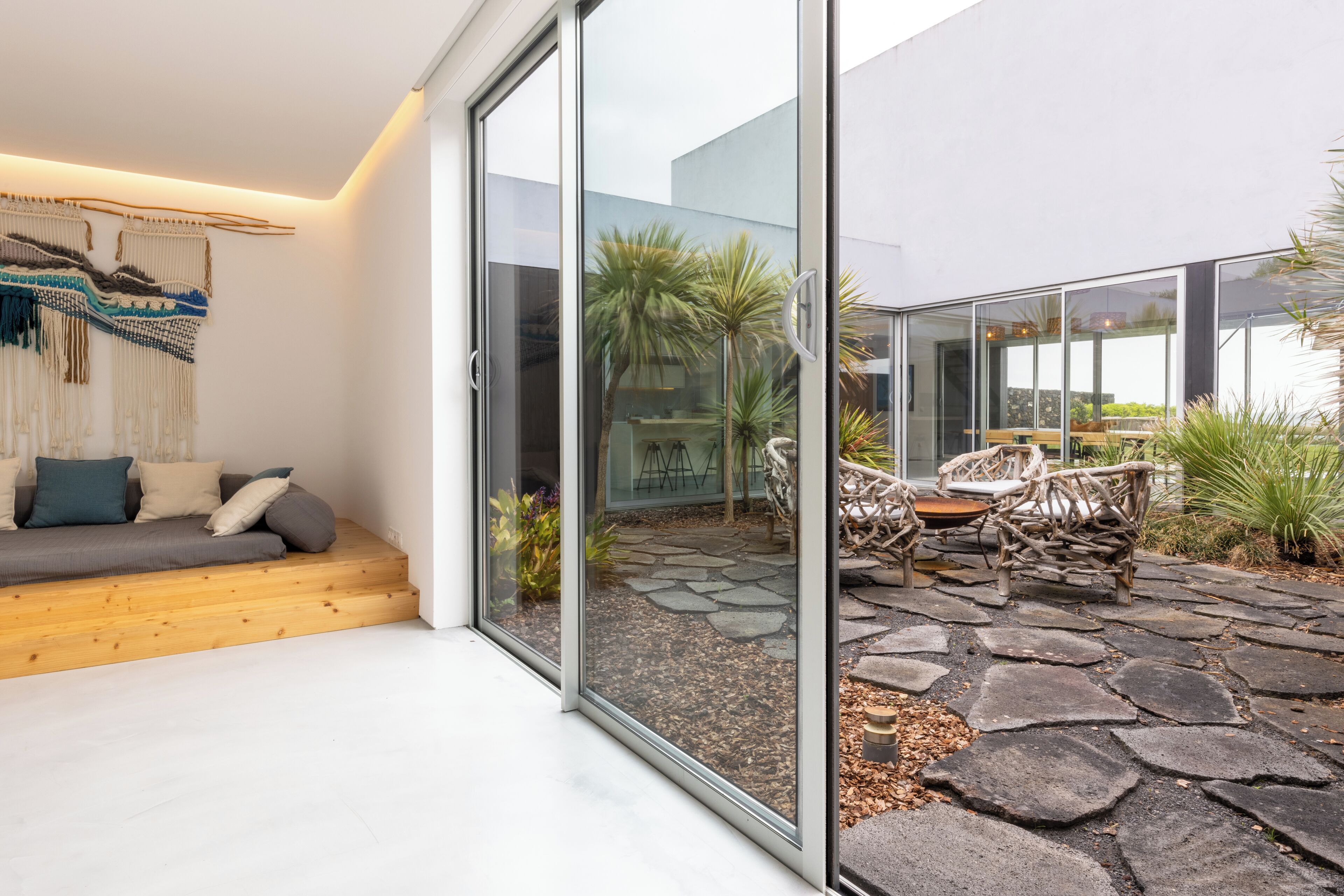 A modern interior with a glass door leading to an outdoor patio area featuring a stone floor, wooden furniture, and potted plants.