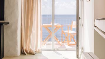 A room with a view of the sea, a sliding glass door, a wooden table and chairs, a bench, and a television on a stand.