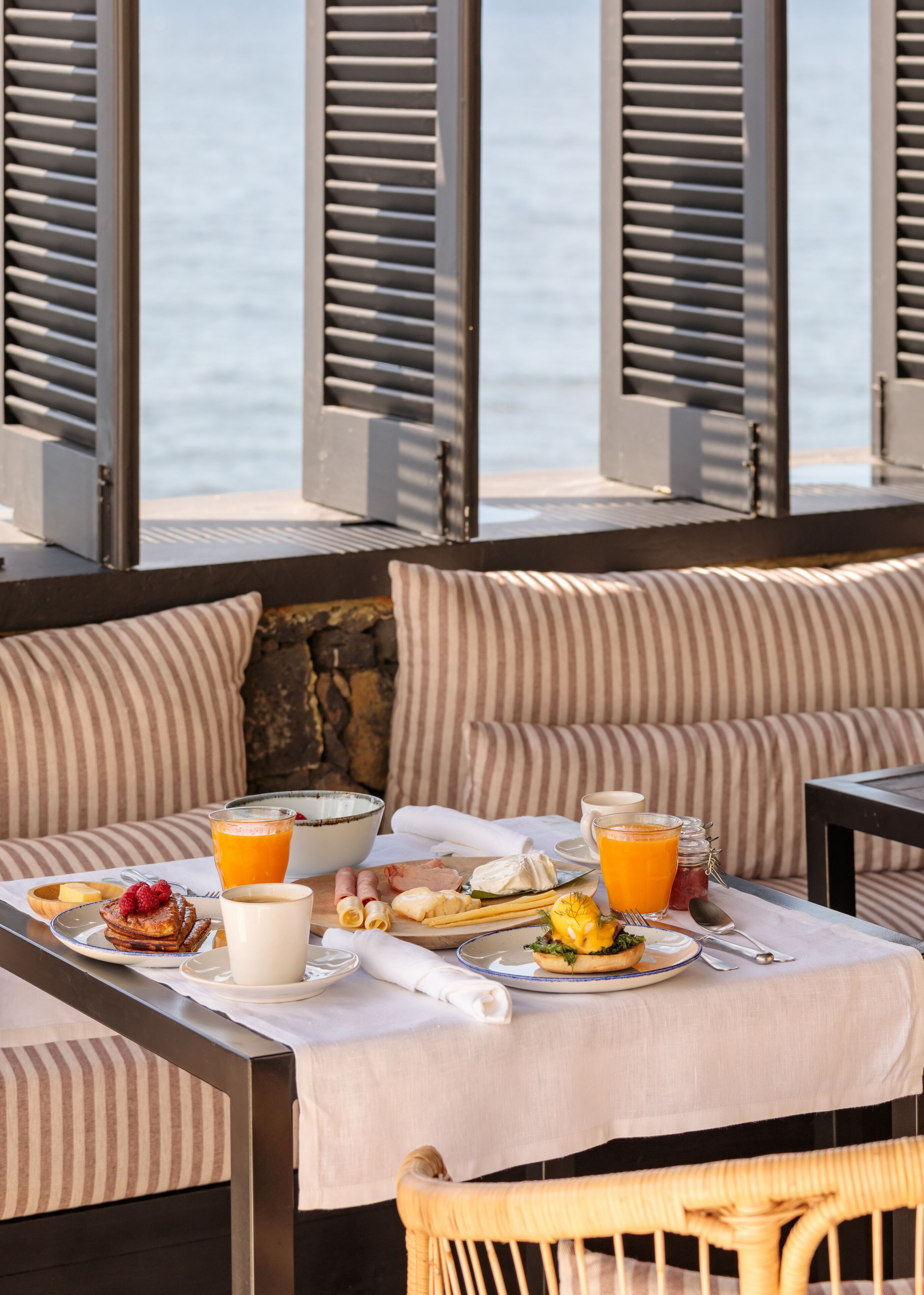 A breakfast setup with a table, striped cushions, and a view of the sea.