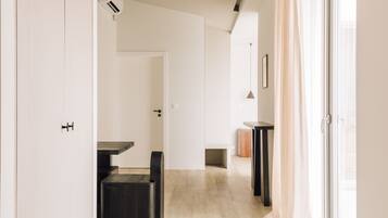 A hallway with a wooden floor, a black bench, a white door, and a small table with a light fixture above it.