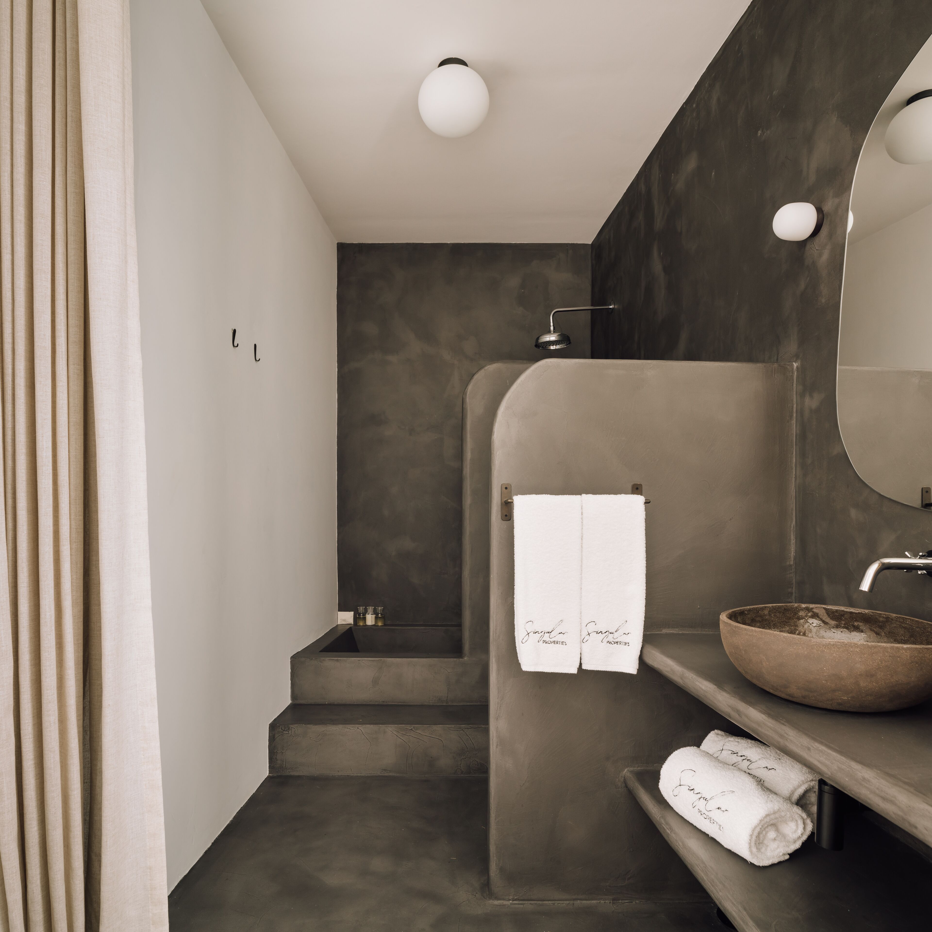 Un baño moderno con un lavamanos de hormigón, un espejo grande y un perchero para toallas.